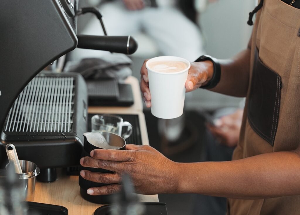 Latte Art and Milk Pitcher | Barista holding a finished latte with latte art next to a milk pitcher at a catered espresso bar