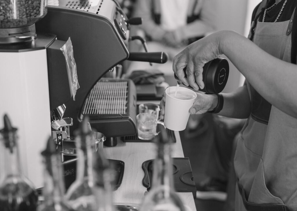 Black and white close-up of steamed milk being poured into a cup at a catered espresso bar